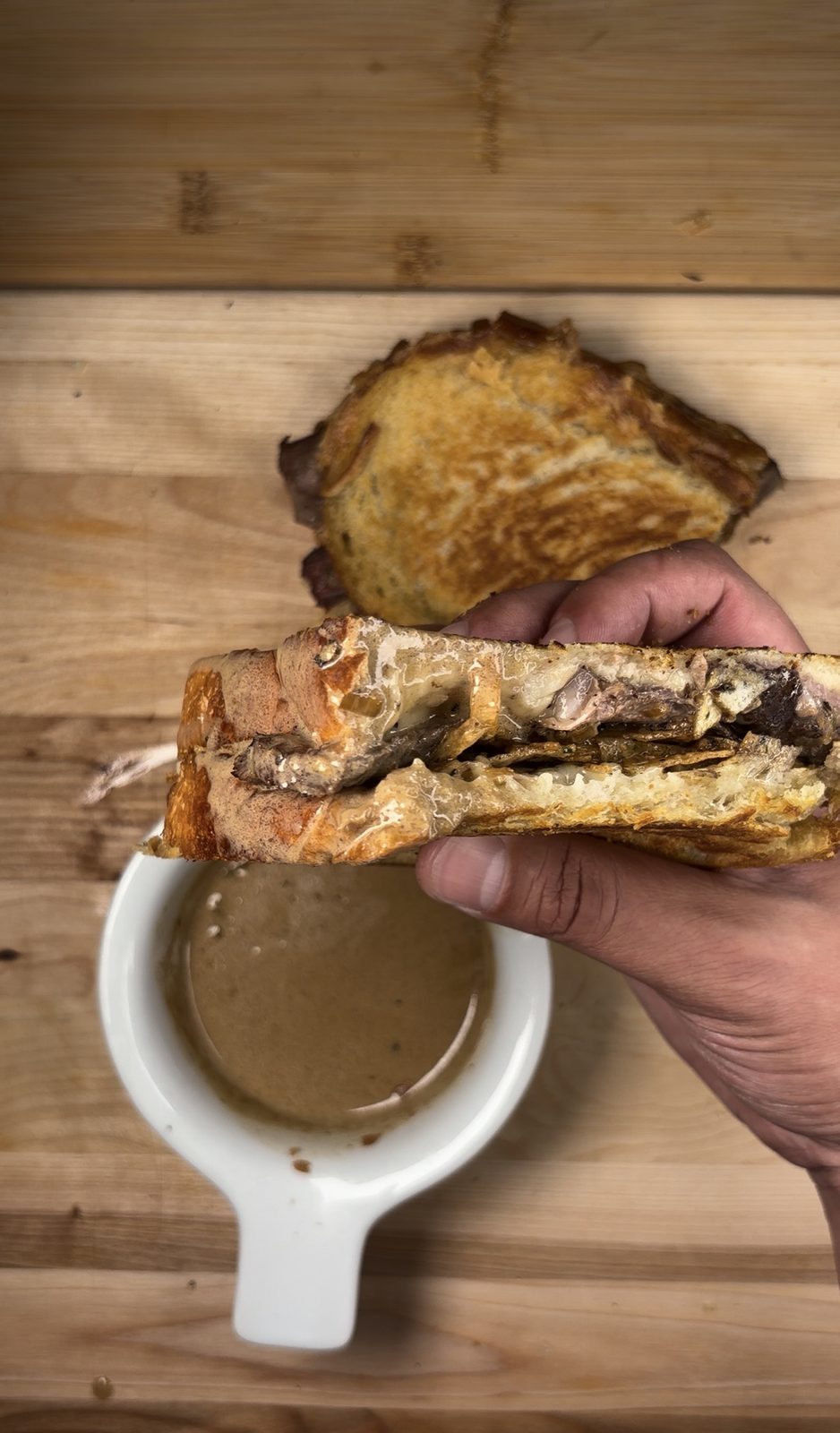 A half of the finished grilled cheese being dunked into a white jug of peppercorn sauce