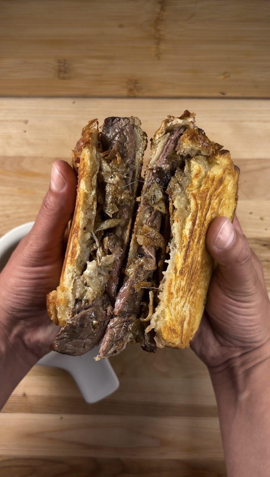 Two halves of a steak frites grilled cheese held to camera, gruyère and shoestring fries visible in the cross-section
