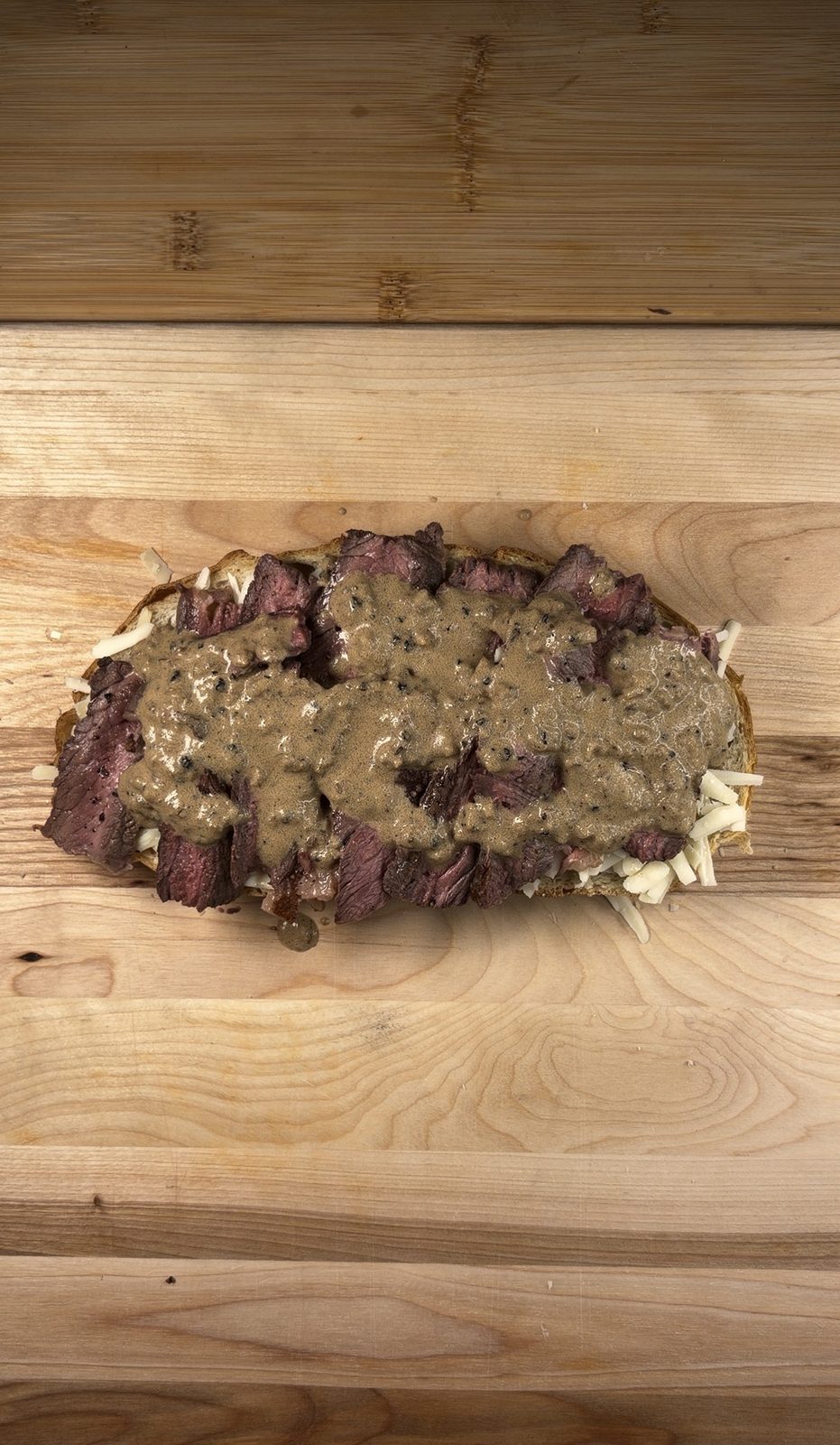 Peppercorn sauce poured over sliced medium-rare steak layered on cheese and sourdough
